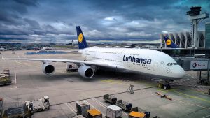 Abbildung eines Flughafens und Flugzeugs mit Lufthansa Aufschrift. Der Himmel ist mit grauen Wolken bedeckt.